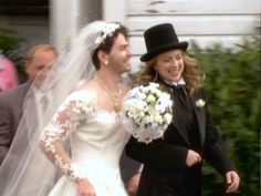 the bride and groom are walking down the street in their wedding attire, with one man wearing a top hat