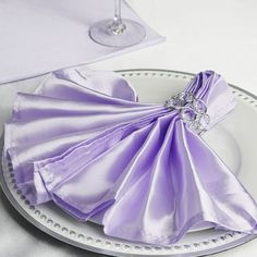 purple napkins are folded on a white plate with silver rimmed wine glass and place setting