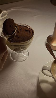 someone is dipping some kind of dessert in a glass bowl next to two cups of coffee