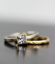 three gold and silver wedding bands with a princess cut diamond in the middle on a table