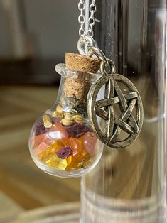 a glass jar filled with lots of different colored rocks and stones on a metal chain