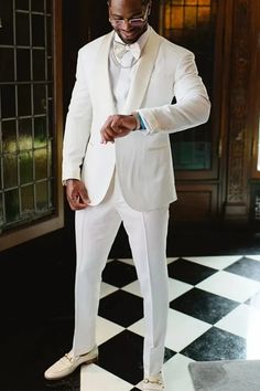 a man in a white tuxedo standing on a black and white checkered floor