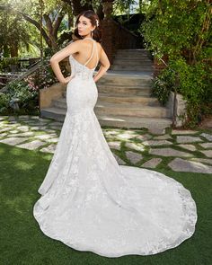 a woman in a white wedding dress standing on the grass with her back to the camera