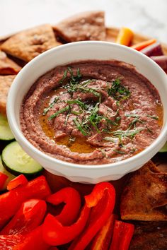 a white bowl filled with dip surrounded by sliced vegetables and crackers