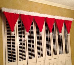 red and white santa hats hanging from the side of a window in front of shutters