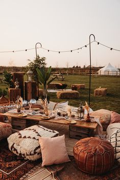 This image shows an outdoor wedding dinner table set up. The image shows a boho vibe. With a low level table in the middle, with a cream table runner, vases with dried flowers, tableware, glassware and rustic wooden tea light candle holders. . Surrounding the table are Moroccan floor cushions and vintage rugs. In the background are wooden plinths displaying a french style lantern and potted trees. Rustic Wedding Furniture, Boho Wedding Furniture, Outdoor Wedding Rugs, Boho Wedding Rugs, Casual Seating Wedding, Floor Seating Wedding, Bohemian Wedding Decorations Outdoor, Casual Farm Wedding, Outdoor Wedding Furniture