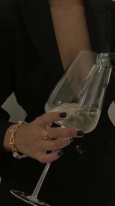 a woman holding a wine glass in her right hand and wearing a gold bracelet on her left wrist