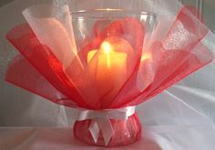 a red vase with a lit candle in it on a white cloth covered tablecloth