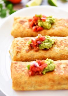 three burritos on a plate with guacamole and tomatoes in the background