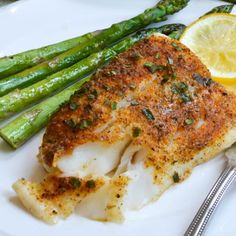 a white plate topped with fish, asparagus and lemon wedges next to a fork