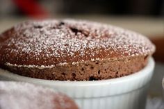 a chocolate cake with powdered sugar on top in a white bowl next to two other cakes