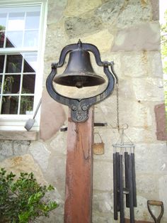 an old fashioned bell hanging from the side of a stone building next to a window