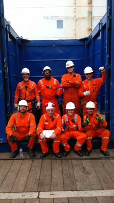 a group of men in orange work suits and hard hats pose for a photo on the deck of a ship