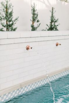 two faucets are connected to the side of a white brick wall and water is running from them