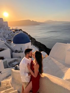 a man and woman are sitting on the steps next to the ocean in front of some buildings