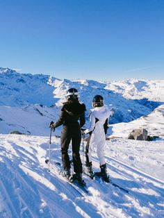 two people standing on top of a snow covered slope