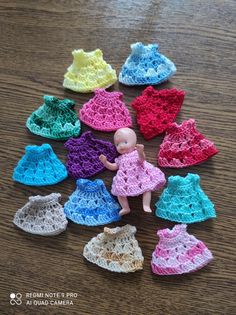 small crocheted doll clothes are arranged on a wooden table with a toy doll in the middle