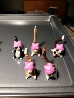 six small figurines in pink hats and sweaters on a baking sheet,