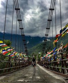 a man riding a motorcycle across a bridge with lots of colorful umbrellas on it