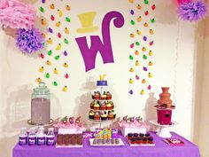 a purple table topped with lots of cupcakes and cake next to a wall