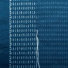 a piece of blue fabric with white stitchs on it and a needle in the middle