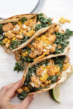 three tacos filled with chicken, corn and spinach on top of a white table