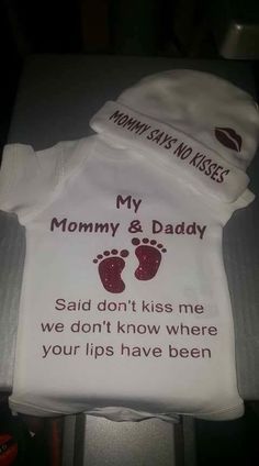 a baby's bodysuit with the words mommy and daddy printed on it, sitting on a table