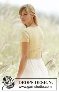 a woman is standing in the grass wearing a yellow knitted sweater and white dress