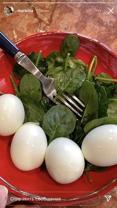 a red plate topped with spinach and hard boiled eggs next to a knife and fork