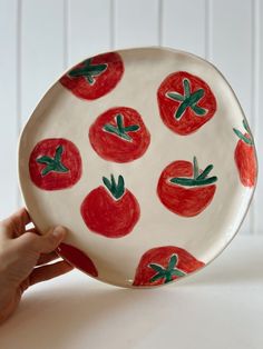 a hand holding a plate with tomatoes painted on it