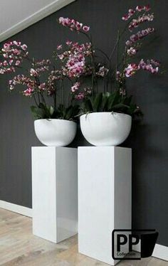 two white vases with flowers in them against a black and gray wall behind it