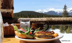 a plate with a burger and salad on it next to a glass of water in front of some mountains