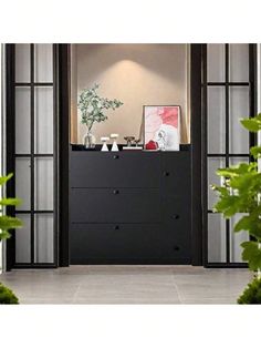 a black dresser sitting inside of a living room next to a plant and potted tree