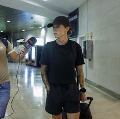 a man and woman walking through an airport holding microphones in their hands, with luggage behind them