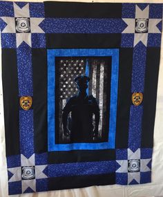 a blue and black quilt with a man standing in front of an american flag