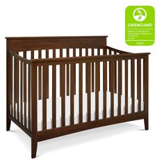 a wooden crib with white bedding and greenguard stickers on the side