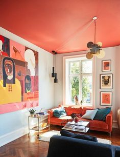 a living room with orange couches and paintings on the wall above them, along with hardwood flooring