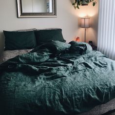 an unmade bed with green sheets and pillows in front of a mirror on the wall