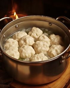 a pot filled with dumplings sitting on top of a wooden table next to a lit candle