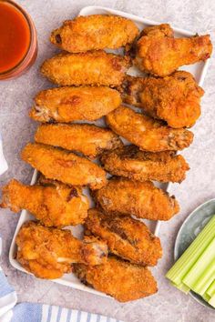 chicken wings and celery sticks on a plate next to a cup of sauce