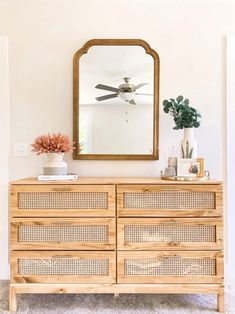 a wooden dresser sitting next to a mirror on top of a white wall in a living room