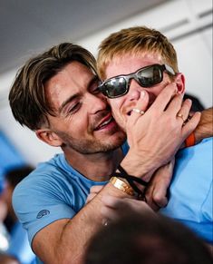 two men who are hugging each other and one has his eyes closed while the other is wearing sunglasses