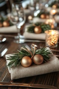 a place setting with silver and gold ornaments on linen napkins, pine needles and candles