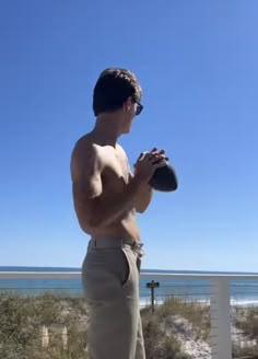 a shirtless man standing on the beach holding a frisbee in his hand