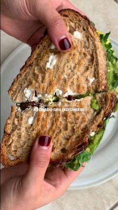 a hand holding a sandwich with lettuce and feta cheese on the side