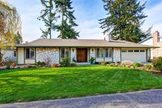 a house that has grass in front of it and trees around the yard with flowers on the lawn