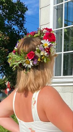 a woman wearing a flower crown in front of a window with her back to the camera