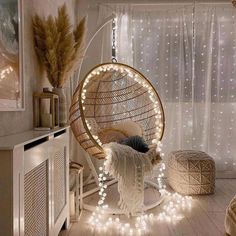 a hanging chair with lights around it in a room that has white curtains and wooden floors