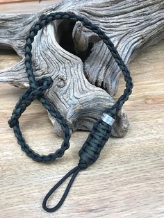 a black cord with a silver clasp on it sitting next to a piece of driftwood