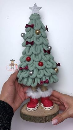 a hand holding a knitted christmas tree on top of a piece of wood with red and white shoes